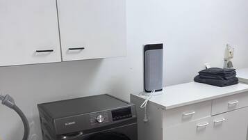 A laundry area with a washing machine, a dryer, a small table with a speaker, and a pink trash bin.