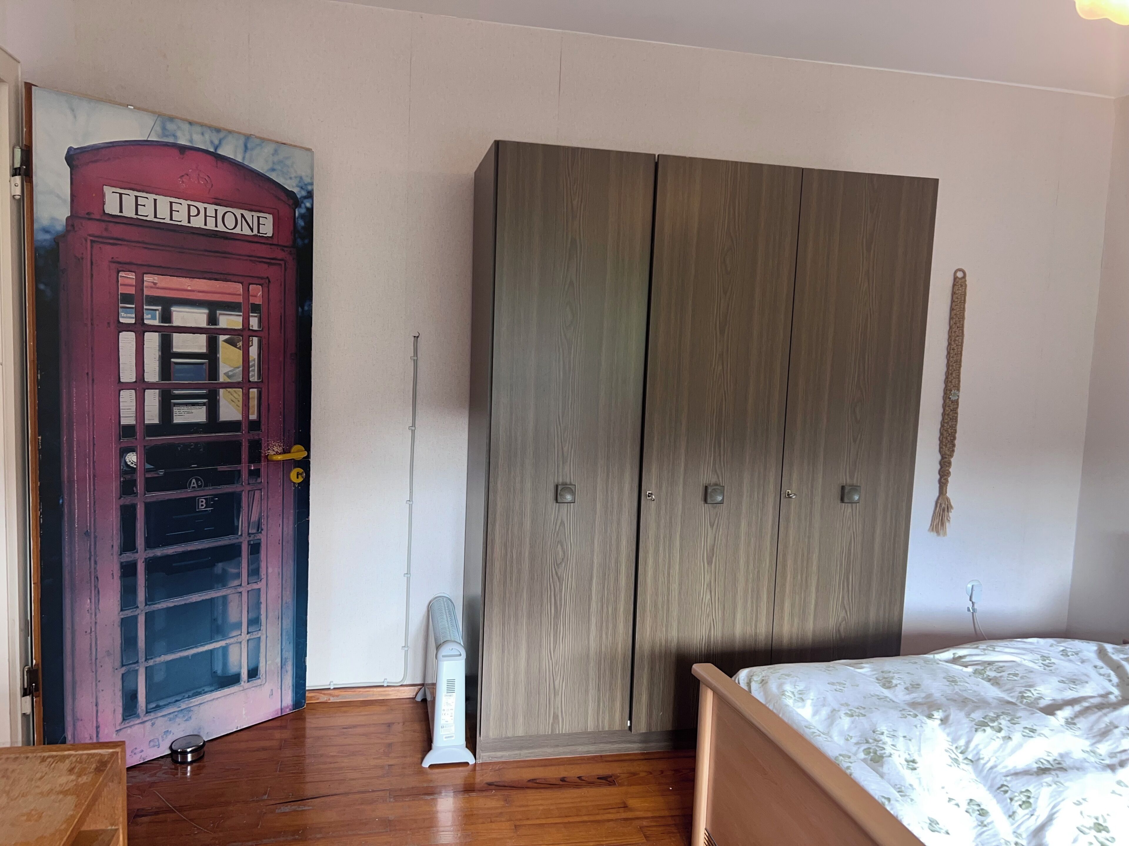 Een slaapkamer met een bed, een kledingkast, een radiator en een deur met een muurschildering van een telefooncel.