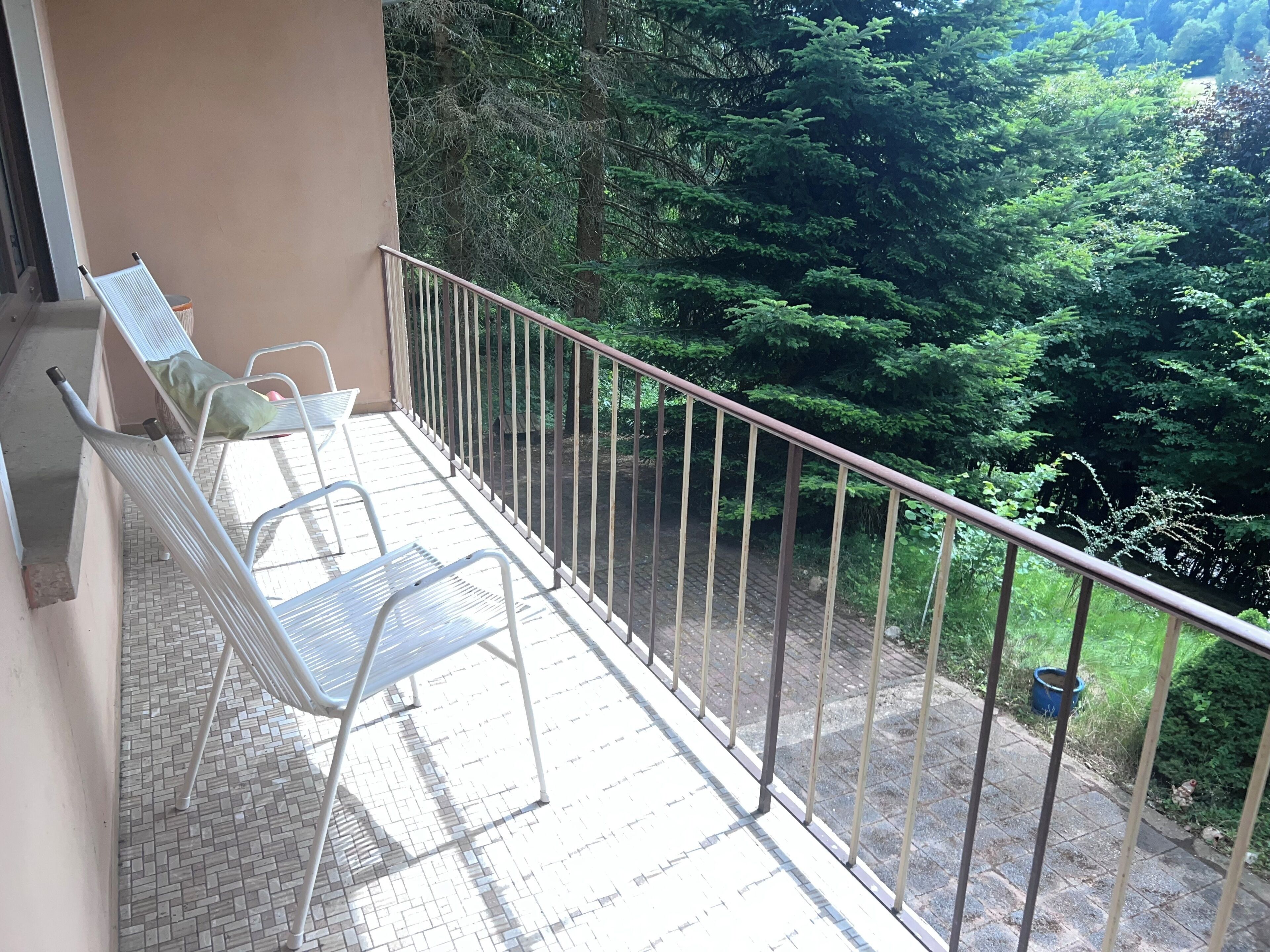 Ein Balkon mit Metallstühlen, gefliestem Boden und Blick auf dichtes Grün.