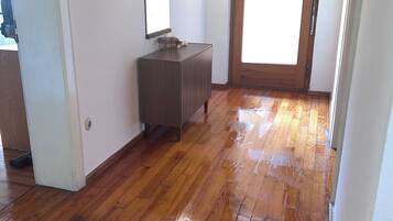 Una habitación con piso de madera, una puerta de madera y una pared blanca con un espejo.