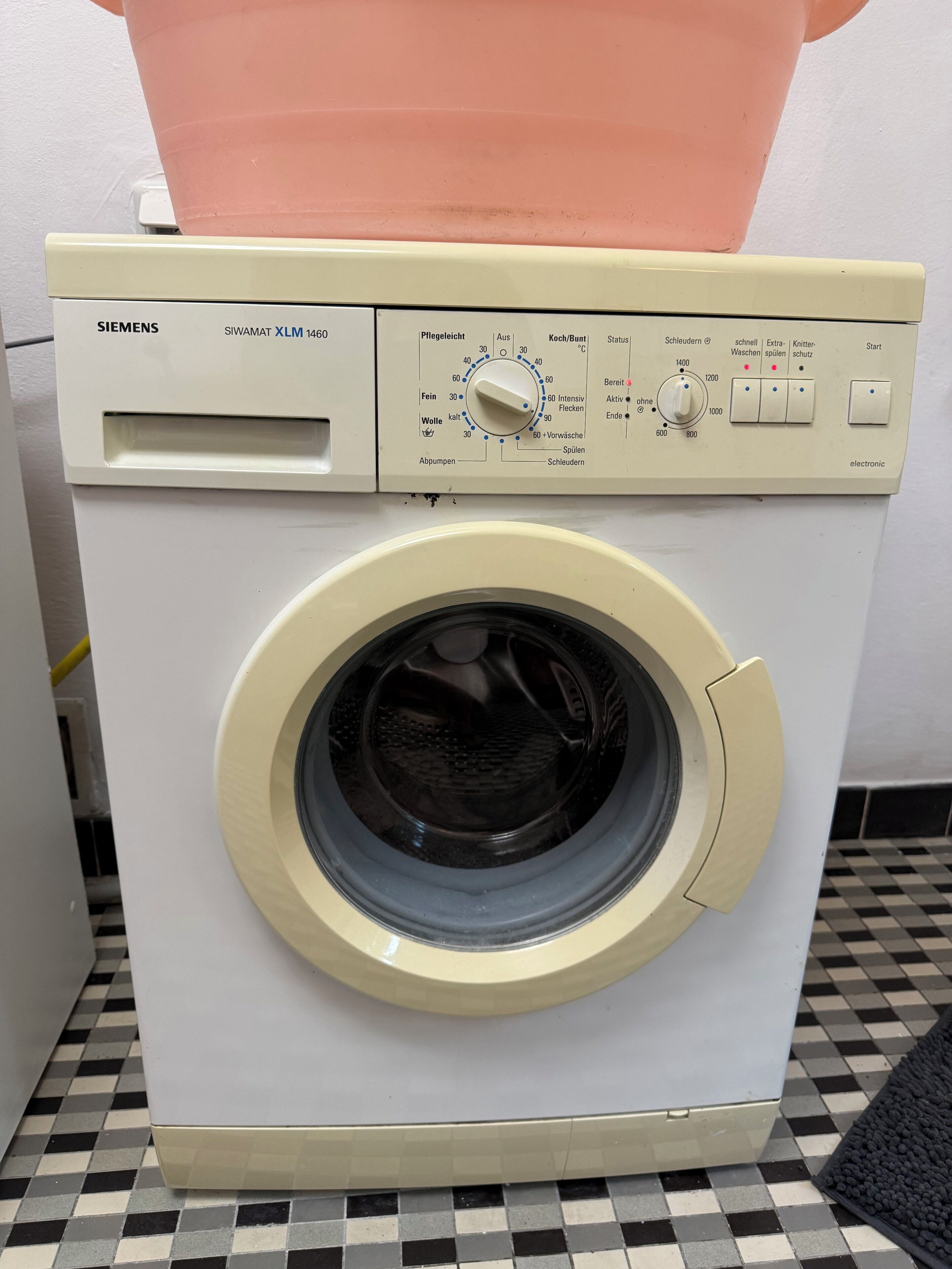 Máquina de lavar roupa Siemens SIWAMAT XLM 1460 de abertura frontal, com painel de controle, topo transparente e chão xadrez.