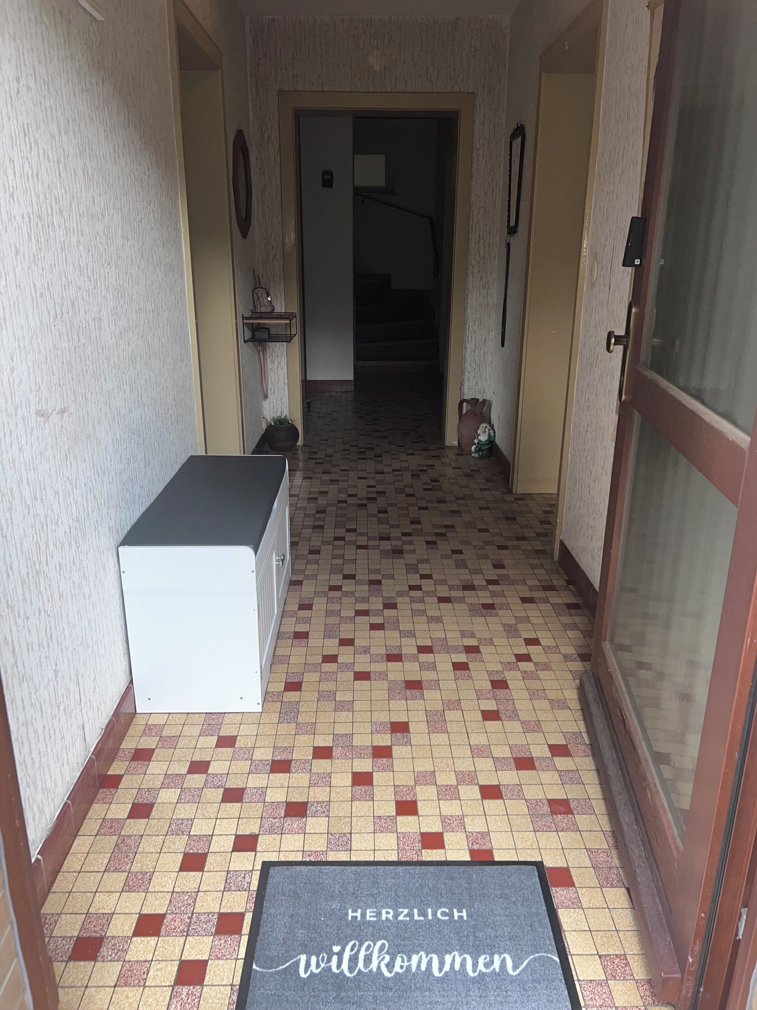 Ein Korridor mit Schachbrettboden, einer Fußmatte, einem weißen Schrank und einer Tür mit Glasfenster.
