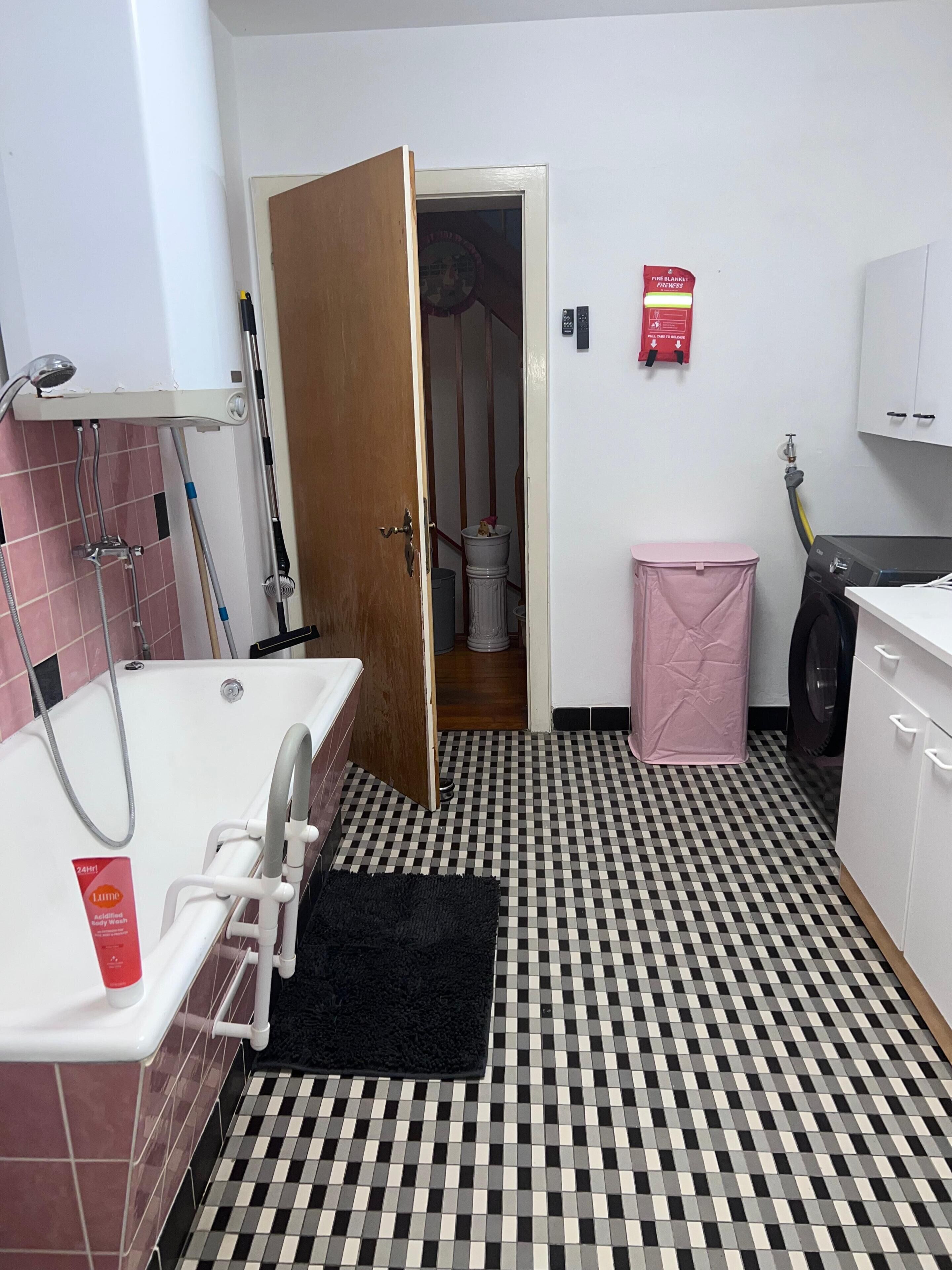 A bathroom with a bathtub, a shower, a toilet, a washing machine, and a pink trash bin.