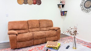 Un salon avec un canapé marron, un jeu de dames, un vase avec des branches, un tapis à motifs et des décorations murales.