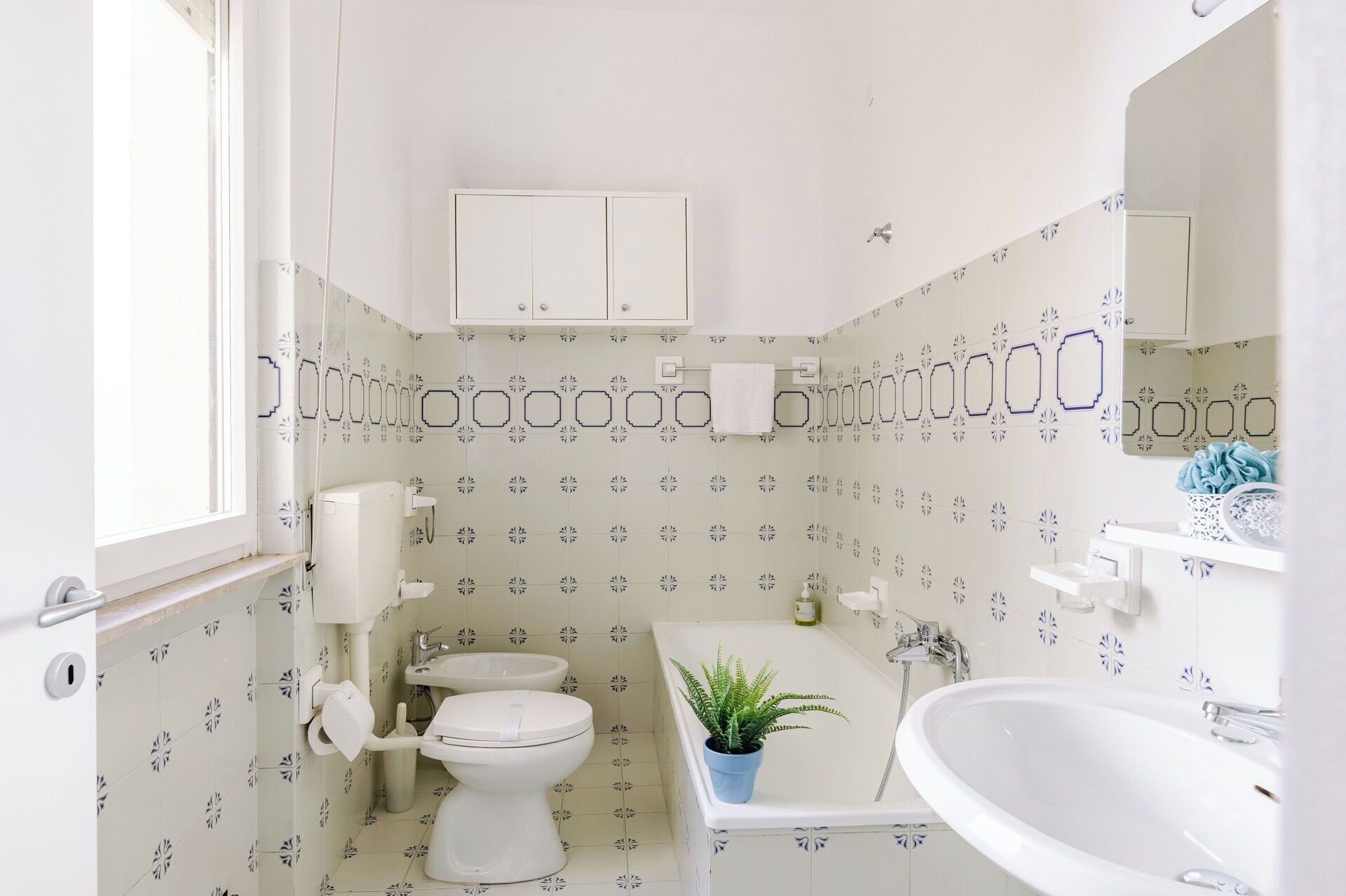 A bathroom with a toilet, sink, bathtub, and a cabinet above the toilet.