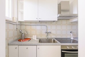 Uma cozinha com pia de aço inoxidável, forno embutido e coifa.