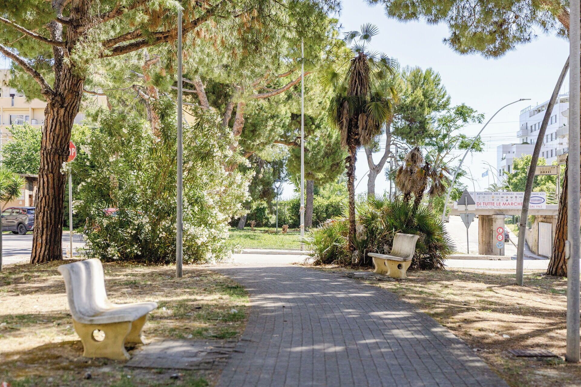 Un sendero pavimentado con bancos, árboles y una señal de parada.