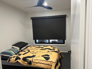 Een slaapkamer met een bed, een raam met een blind, een plafondventilator en een klein raam.