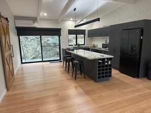 Een moderne keuken met een centraal eiland, donkere kasten en een groot raam met uitzicht op bomen.