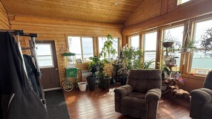 Interior de una cabaña de madera con un sofá, sillas, una bicicleta y plantas en macetas.