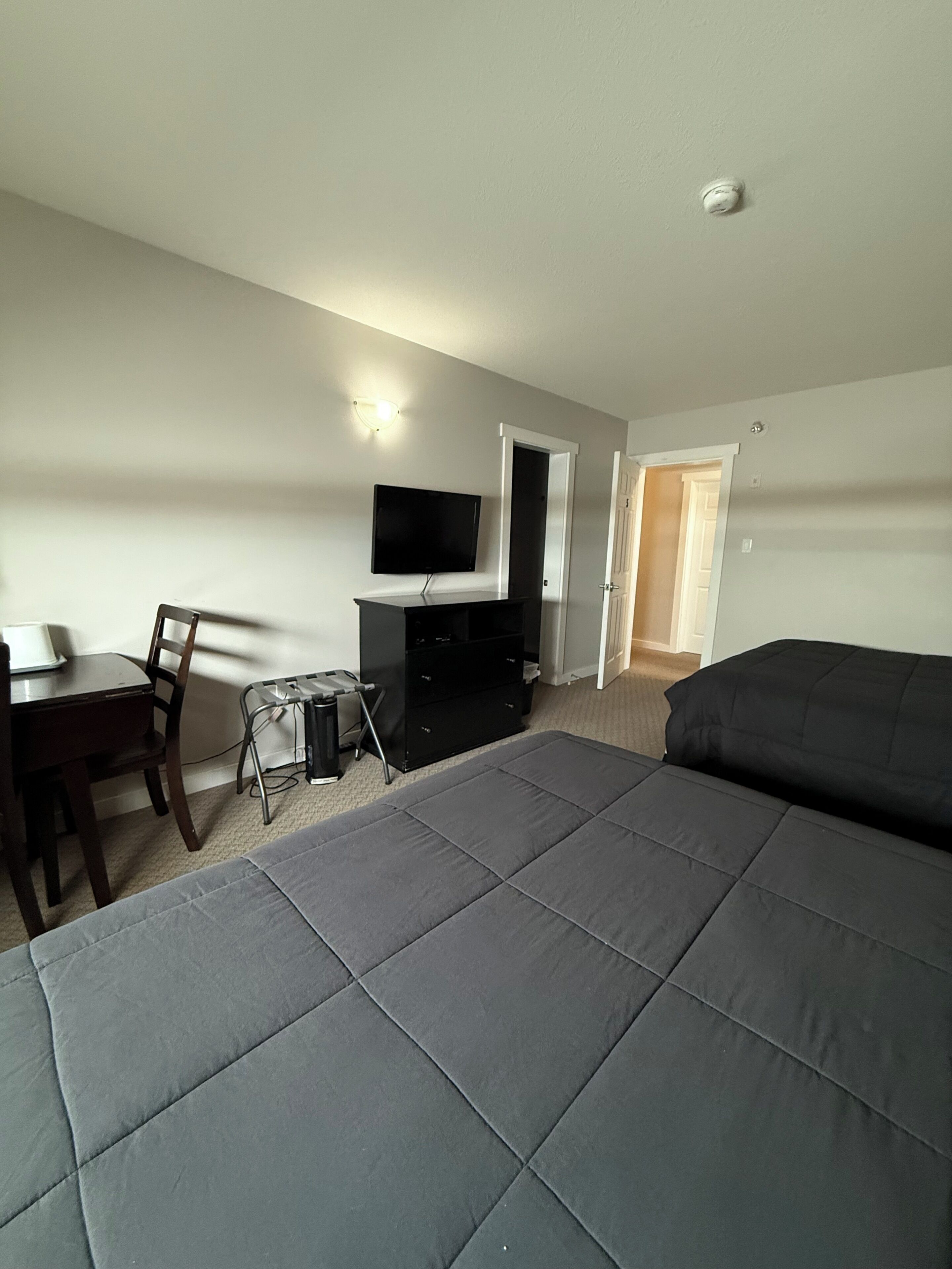 Een slaapkamer met een bed, bureau, stoel, televisie en een deur.