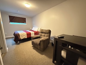 Een slaapkamer met een bed, een stoel, een bureau en een raam.