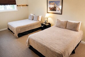 A room with two beds, a nightstand with a lamp, a framed picture on the wall, and a window with a curtain.