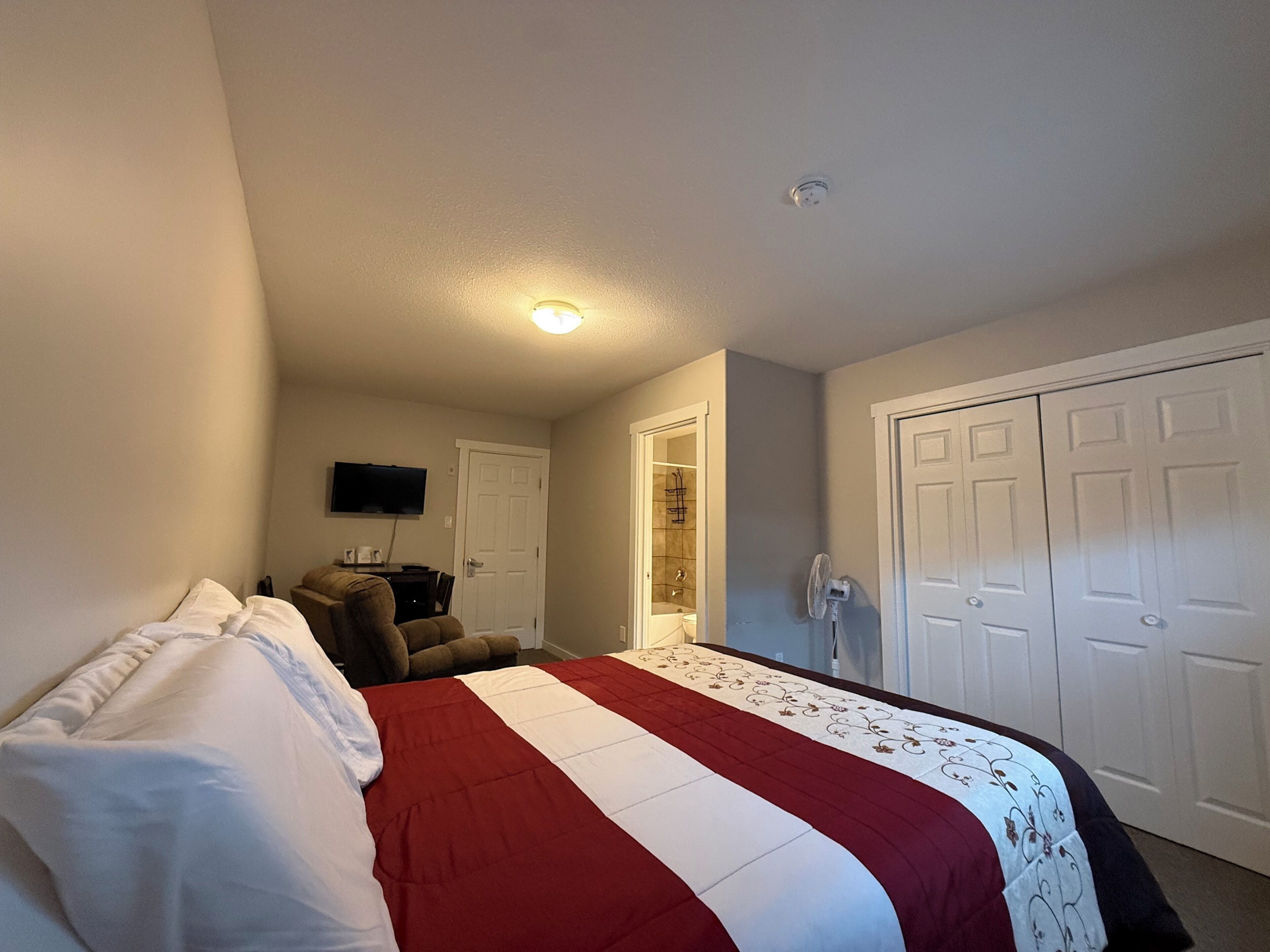 Een slaapkamer met een bed, een televisie aan de muur, een deur en een kast.