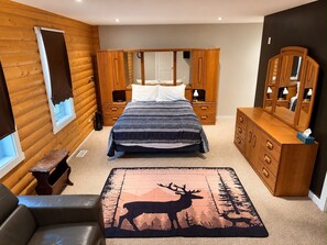 A bedroom with a bed, wooden wardrobe, dresser, and a deer rug.
