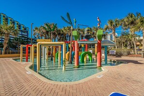 Ein Wasserspielbereich mit bunten Elementen, Palmen und blauem Himmel.