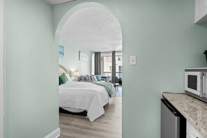 A bedroom with a bed, a nightstand, and a window. - NEW Remodel-Private Balcony-Elevator-Pool-King bed (Myrtle Beach)
