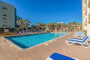 A swimming pool with lounge chairs, palm trees, and a building in the background. - NEW Remodel-Private Balcony-Elevator-Pool-King bed (Myrtle Beach)