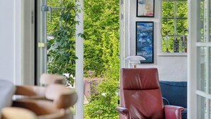 Una habitación con una silla roja, un banco de madera y vistas a la vegetación a través de un ventanal.