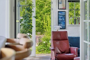 Una habitación con una silla roja, un banco de madera y vistas a la vegetación a través de un ventanal.