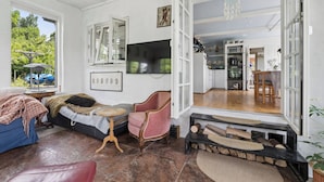 Un espacio habitable de concepto abierto con un sofá, un sillón rosa, un televisor y una cocina visible a través de una puerta abierta.
