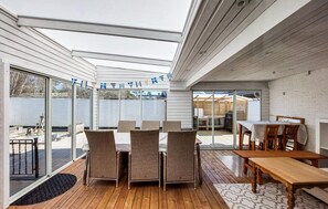 A covered patio area with wicker furniture, a wooden table, and a grill.