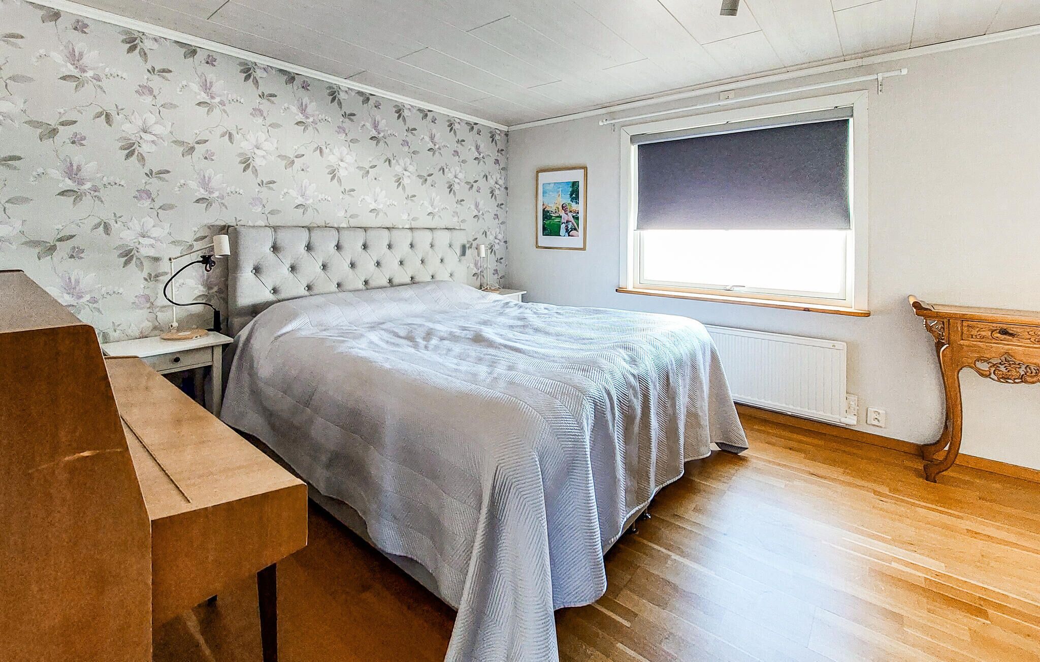 Une chambre à coucher avec un lit, un bureau, un radiateur, une fenêtre et un tableau accroché au mur.