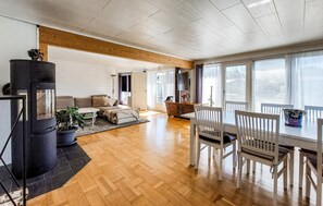 A spacious living room with a wooden floor, a sofa, a dining table with chairs, and a black heater. - 4 bedroom cozy home in Mellbystrand (Mellbystrand)
