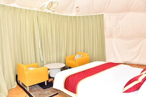 Ein Zelttyp-Zimmer mit einem Bett, zwei gelben Sesseln, einem kleinen runden Tisch und einem Vorhang.