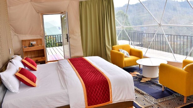 A tent-style room with a bed, yellow chairs, a small table, and a view of mountains. - Hillside Escape Glamping (Kodaikanal)