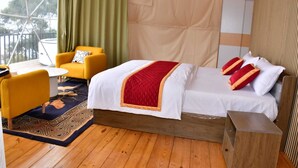 A bedroom with a bed, a yellow armchair, a small table, and a wooden floor. - Hillside Escape Glamping (Kodaikanal)