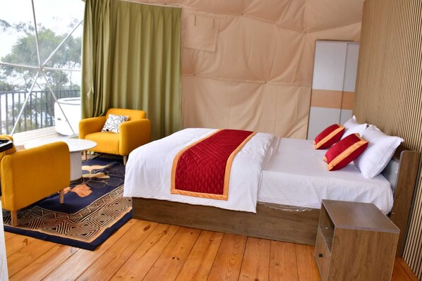 A bedroom with a bed, a yellow armchair, a small table, and a wooden floor.