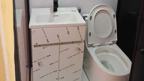 A small bathroom with a toilet, a sink, a mirror, and a shelf with a bottle. - Hillside Escape Glamping (Kodaikanal)