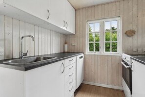 Eine moderne Küche mit weißen Schränken, einer Edelstahl-Spüle und einem Fenster mit Blick auf Grünflächen.