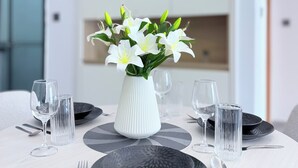 A dining table with a white vase of white flowers, black plates, and clear glasses. - Secure Lavington Apt w/ Pool, Gym & Fast WiFi – 1 Min Walk to Junction Mall (Nairobi)