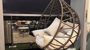 A hanging chair with cushions, a glass partition, and a view of an outdoor seating area. - Secure Lavington Apt w/ Pool, Gym & Fast WiFi – 1 Min Walk to Junction Mall (Nairobi)