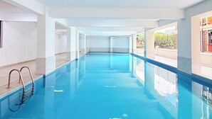 An indoor swimming pool with clear water, a diving board, and a view of the outside. - Secure Lavington Apt w/ Pool, Gym & Fast WiFi – 1 Min Walk to Junction Mall (Nairobi)
