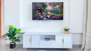 A modern living room with a mounted TV, a white cabinet with gold handles, a potted plant, and a small house-shaped decoration. - Secure Lavington Apt w/ Pool, Gym & Fast WiFi – 1 Min Walk to Junction Mall (Nairobi)
