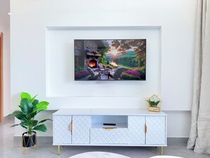A modern living room with a mounted TV, a white cabinet with gold handles, a potted plant, and a small house-shaped decoration. - Secure Lavington Apt w/ Pool, Gym & Fast WiFi – 1 Min Walk to Junction Mall (Nairobi)