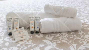 Un lit bien fait, avec des serviettes blanches pliées et plusieurs flacons de produits de soins pour la peau disposés sur une couvre-lit à motifs.
