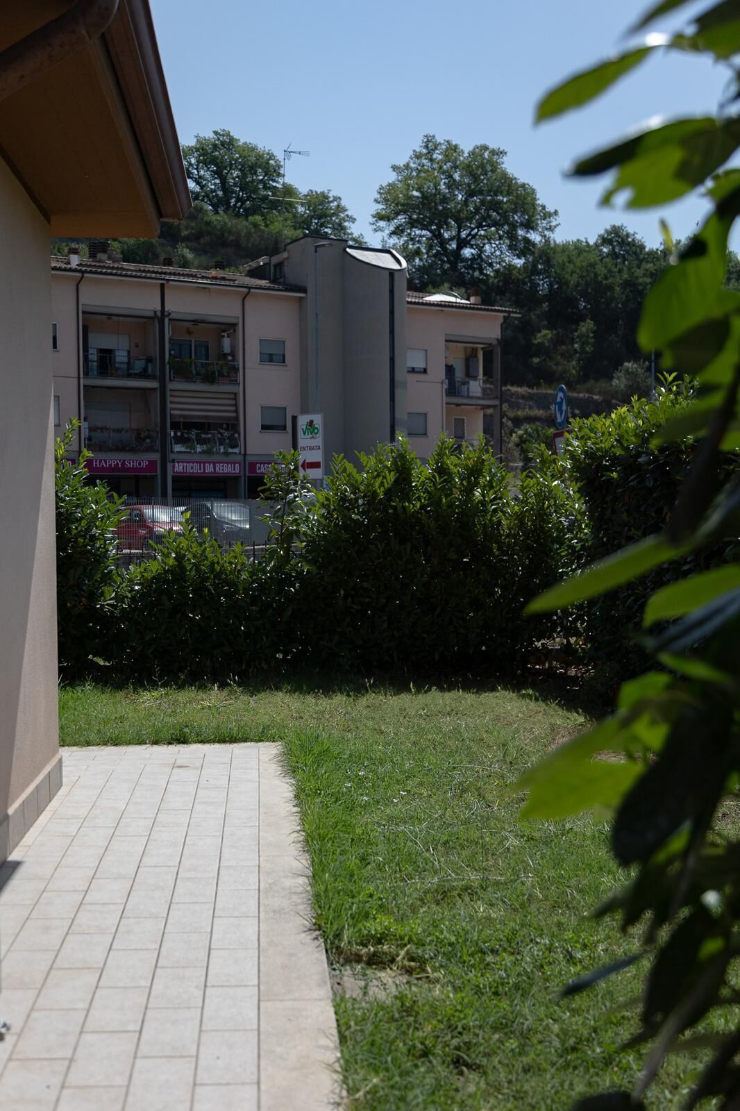 A residential building with a tiled pathway, a hedge, and a sign indicating a 'Happy Shop.'