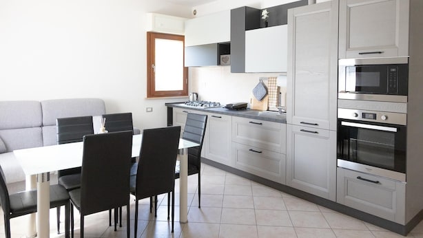 Een moderne keuken met grijze kastjes, een eettafel met stoelen en een inbouwoven.