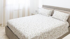Een slaapkamer met een bed, gordijnen, een nachtkastje en een bijzettafeltje.