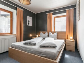 Une chambre à coucher moderne avec un lit en bois, deux tables de chevet, une lampe fixée au mur et une fenêtre avec des rideaux.