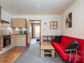 A compact kitchen with modern appliances, a dining area with a red sofa, and a hallway leading to a bedroom.