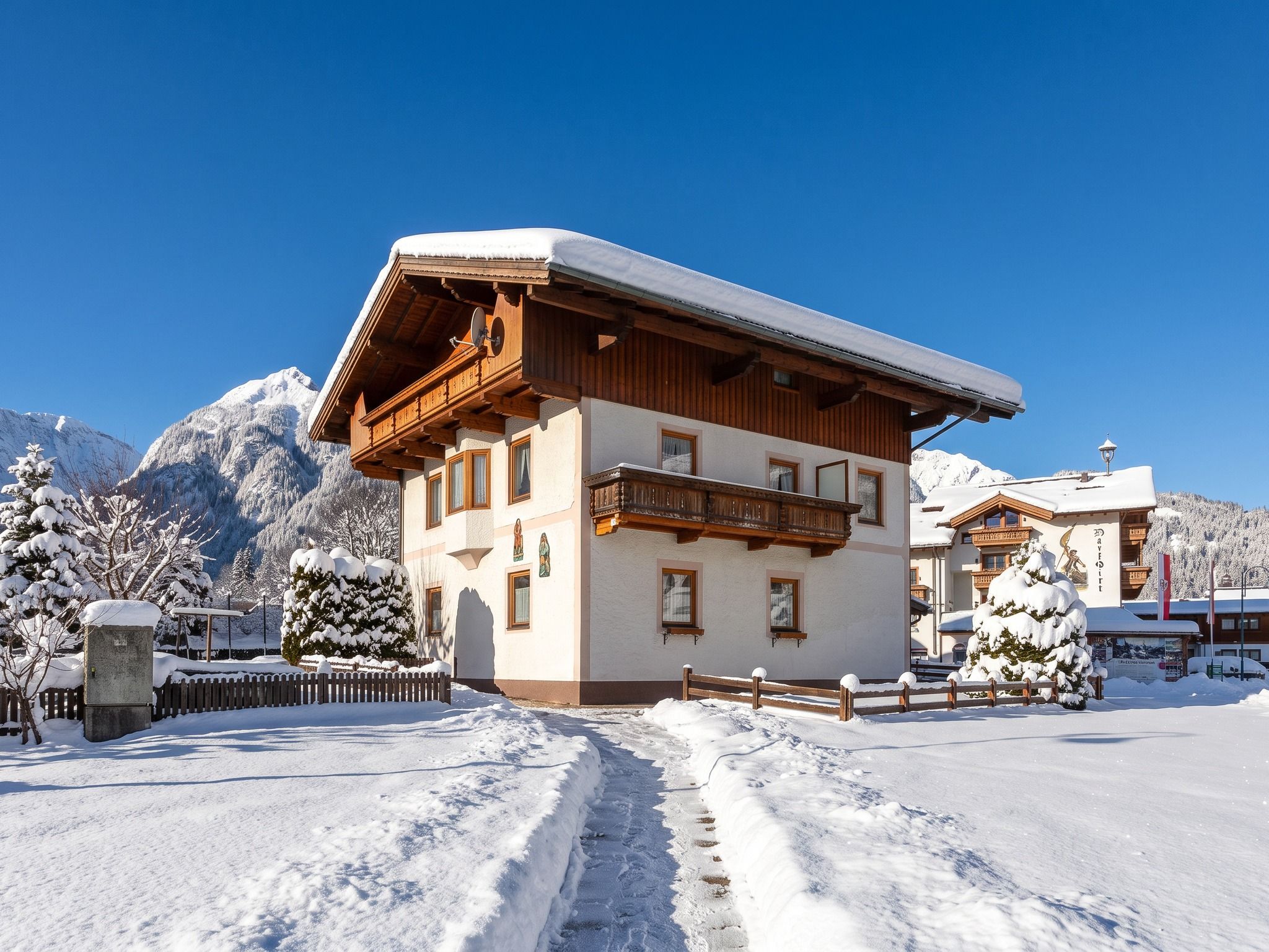 A two-story chalet with a balcony, surrounded by snow-covered trees and mountains.