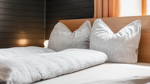 Un lit avec une tête de lit en bois, des oreillers à motifs gris et une couverture blanche.