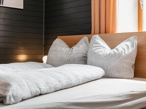 A bed with a wooden headboard, grey patterned pillows, and a white blanket. - Garden apartment only 15 min. walk to the lake (Maurach am Achensee)