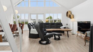 A spacious living area with a black leather sofa, a black recliner, a wooden coffee table, and a TV. Large windows provide natural light and a view of the outside. - Scenic holiday home close to the water (Brenderup)
