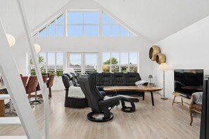 A spacious living area with a black leather sofa, a black recliner, a wooden coffee table, and a TV. Large windows provide natural light and a view of the outside. - Scenic holiday home close to the water (Brenderup)